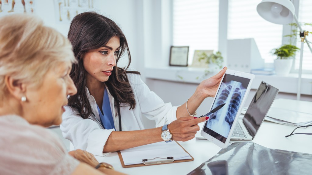 Doctor explaining lung x-ray results on a tablet to an older patient with a smoking problem in a medical clinic